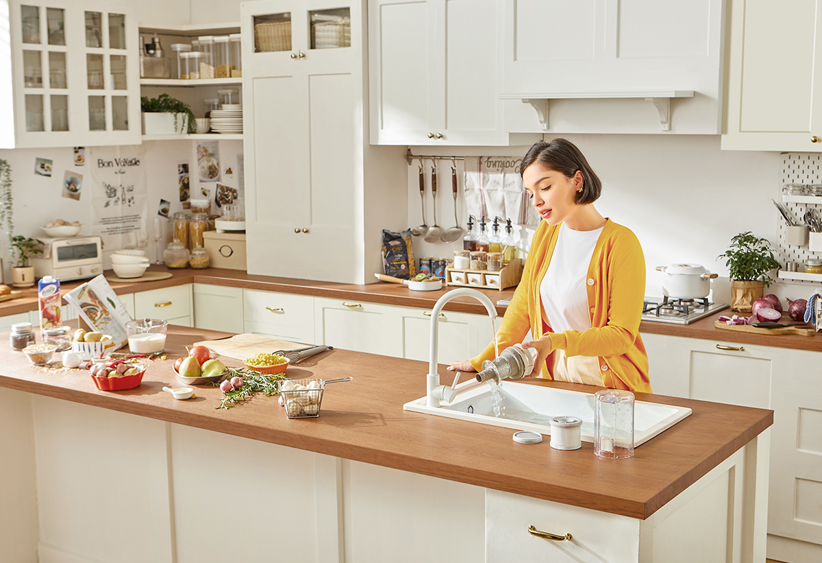 Απεικονίζεται μια γυναίκα να πλένει τα εξαρτήματα της σκούπας στον νεροχύτη.